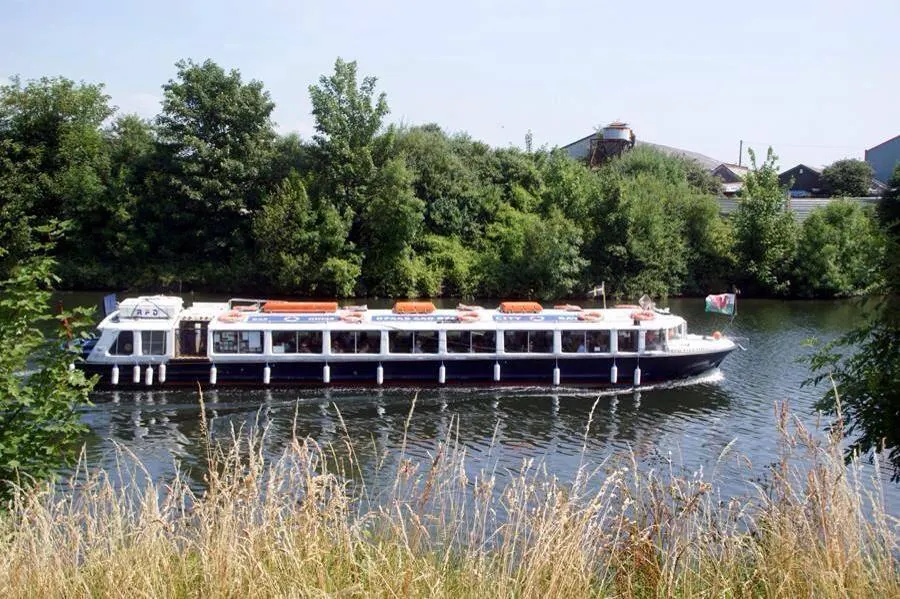 Passenger river cruising boat moored on a waterway, surrounded by trees and reeds.