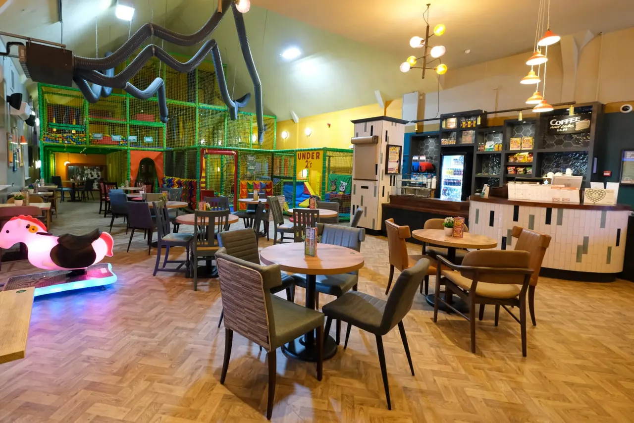 Indoor play venue with seating areas, colourful soft play structures, a service counter and illuminated play equipment.