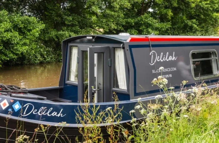 Narrowboat moored beside wildflowers and trees on a canal.