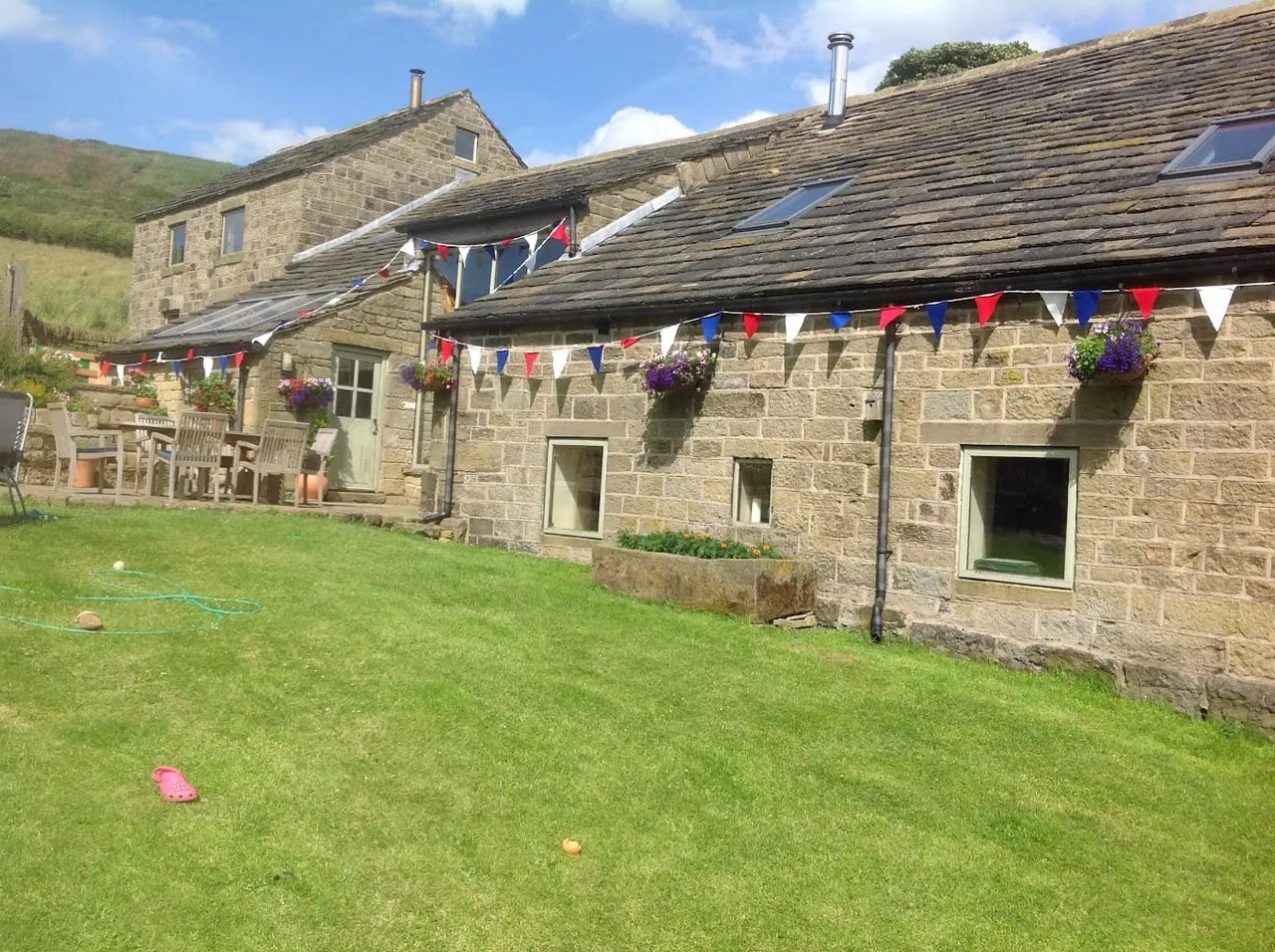 Stone buildings with bunting decorations and a lawn with outdoor games in a rural hillside setting.
