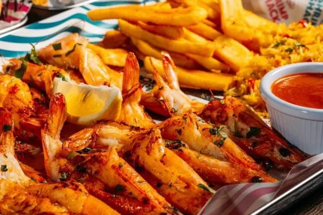 Grilled prawns with lemon and herbs served with chips and red sauce on a striped plate.