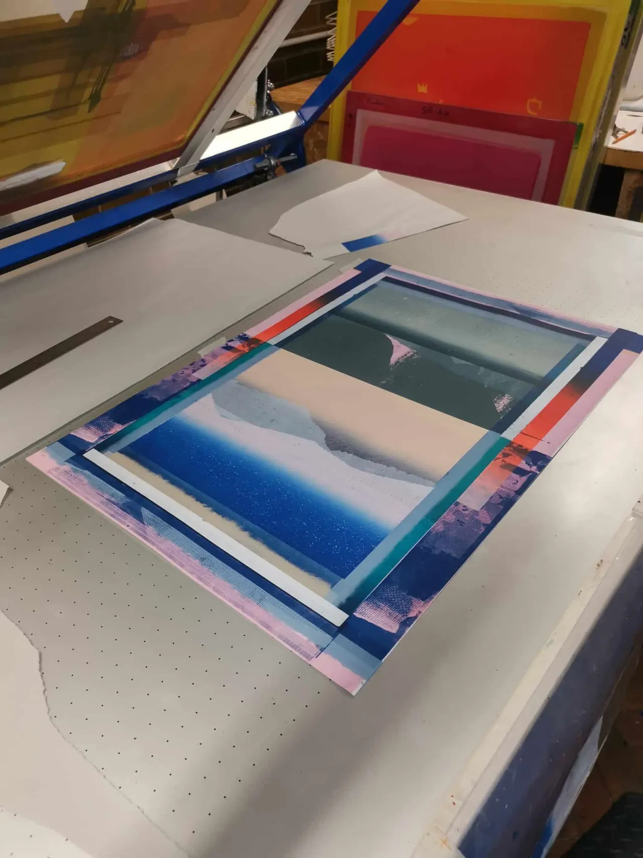 Screen printing artwork in progress on a printing table with blue squeegee and layered color separations.