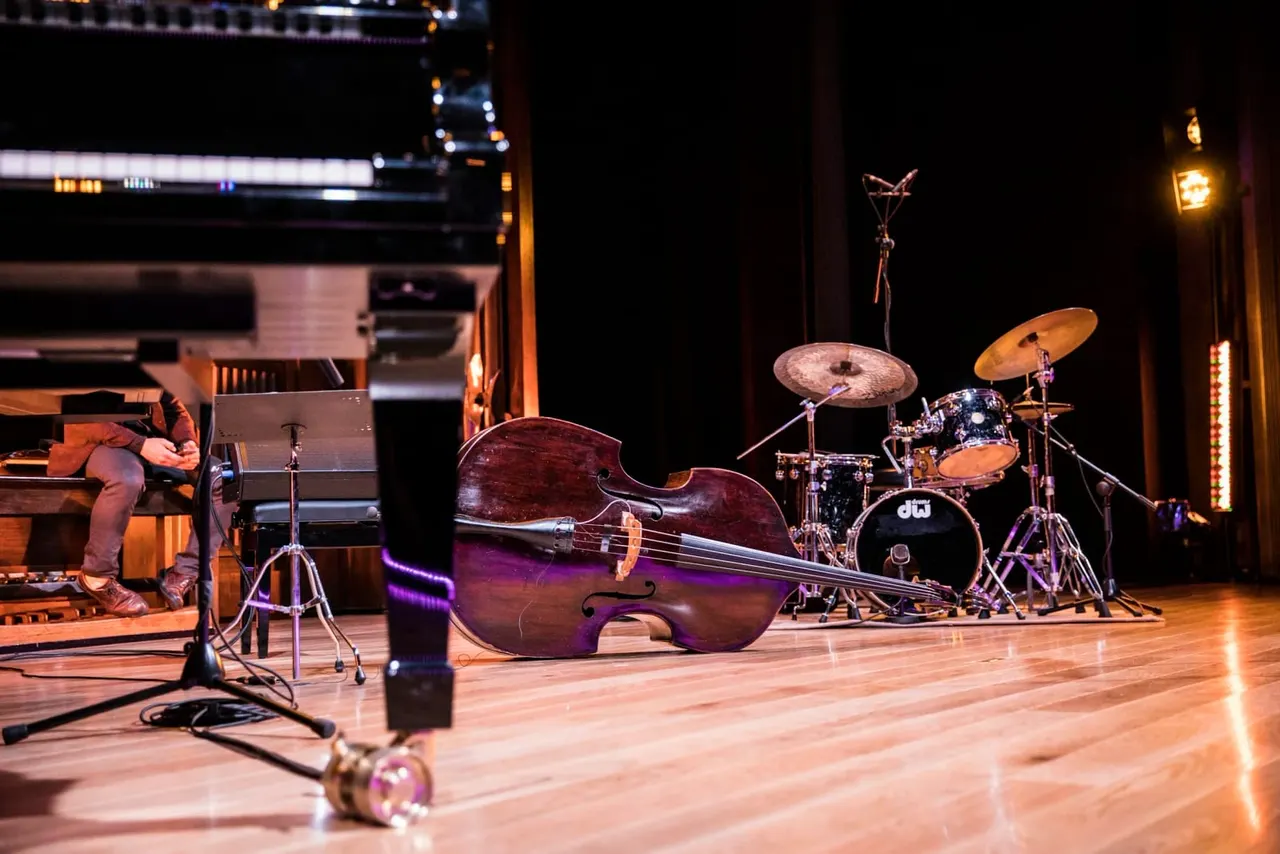 Jazz ensemble performing on stage with cello, drums, and piano under warm stage lighting.
