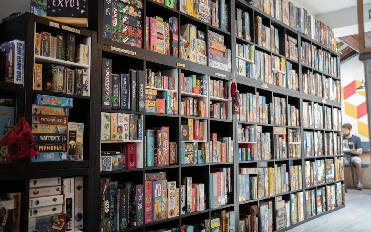 Extensive wall shelving displaying hundreds of colourful board games in boxes, with a visitor browsing on the right.