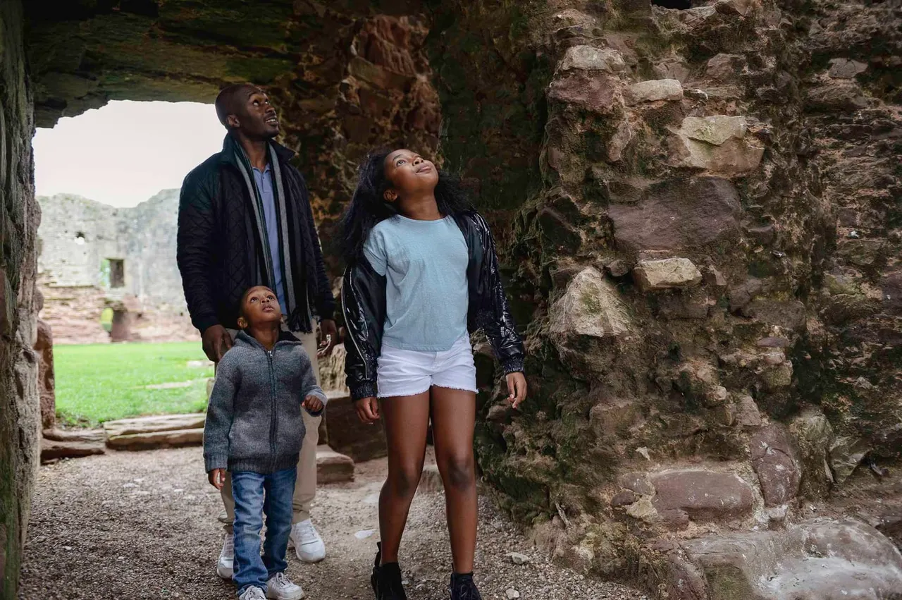 Family exploring ancient stone ruins, looking up at medieval castle walls and archway.