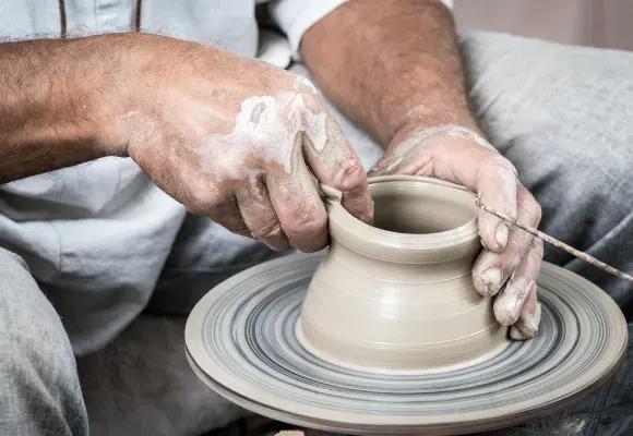 Potter's hands shaping clay on a spinning wheel to form a vessel.