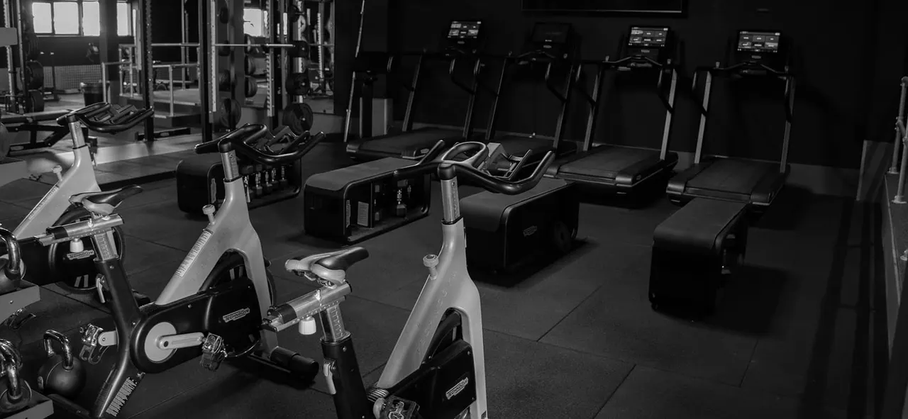 Gym interior with rows of treadmills and exercise bikes, black and white photograph.