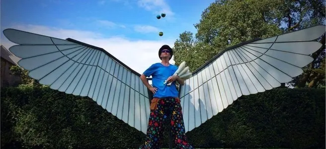 Person juggling while standing between large white wing installations outdoors.