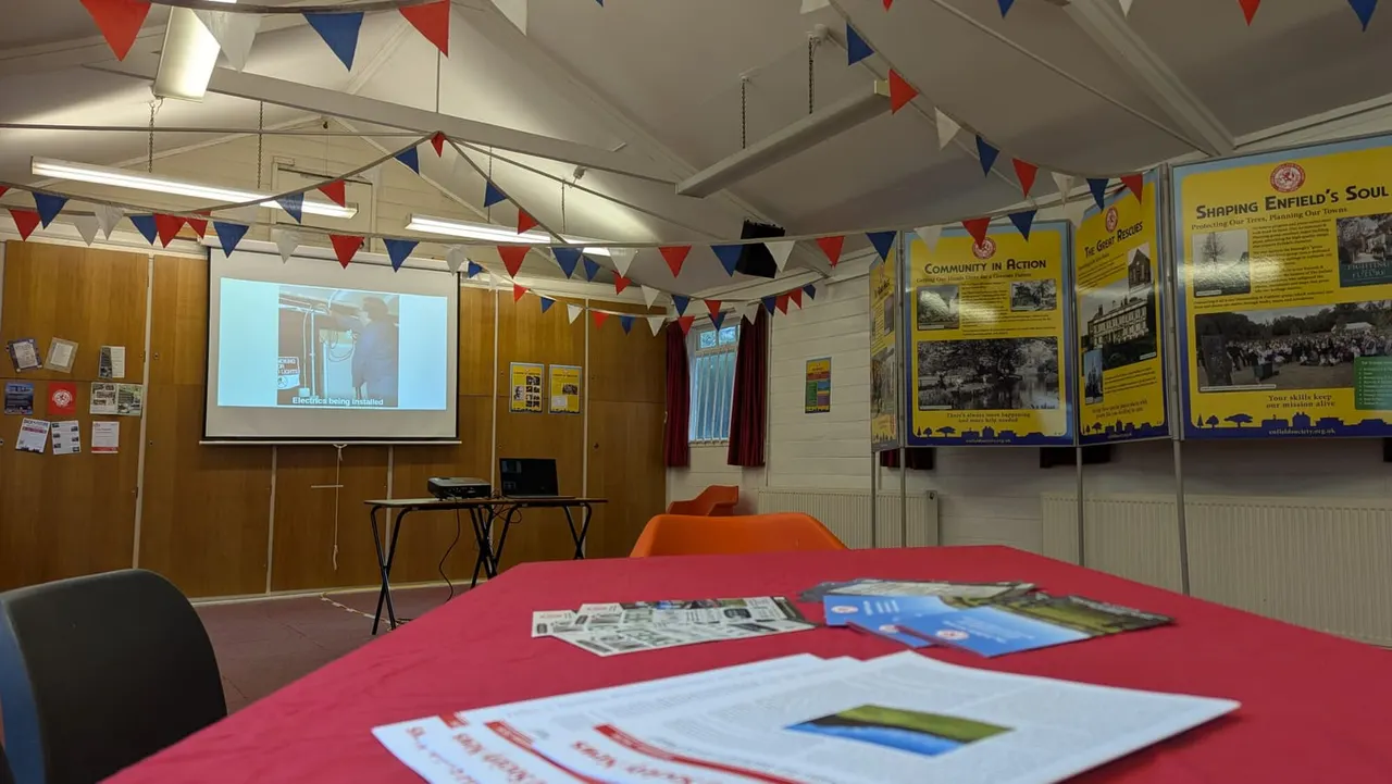 Community hall decorated with red, white and blue bunting, displaying historical exhibition panels and a projection screen showing a presentation.