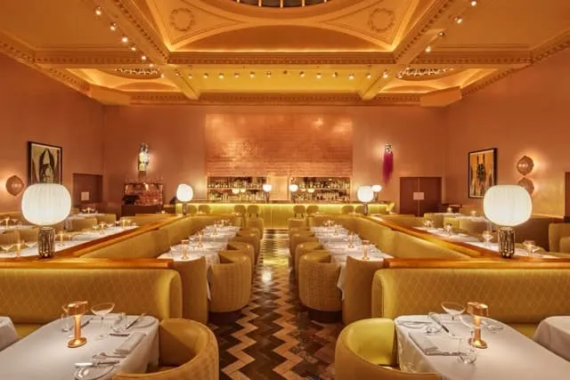 Elegant fine dining restaurant interior with gold banquettes, ornate ceiling, and formally set tables.