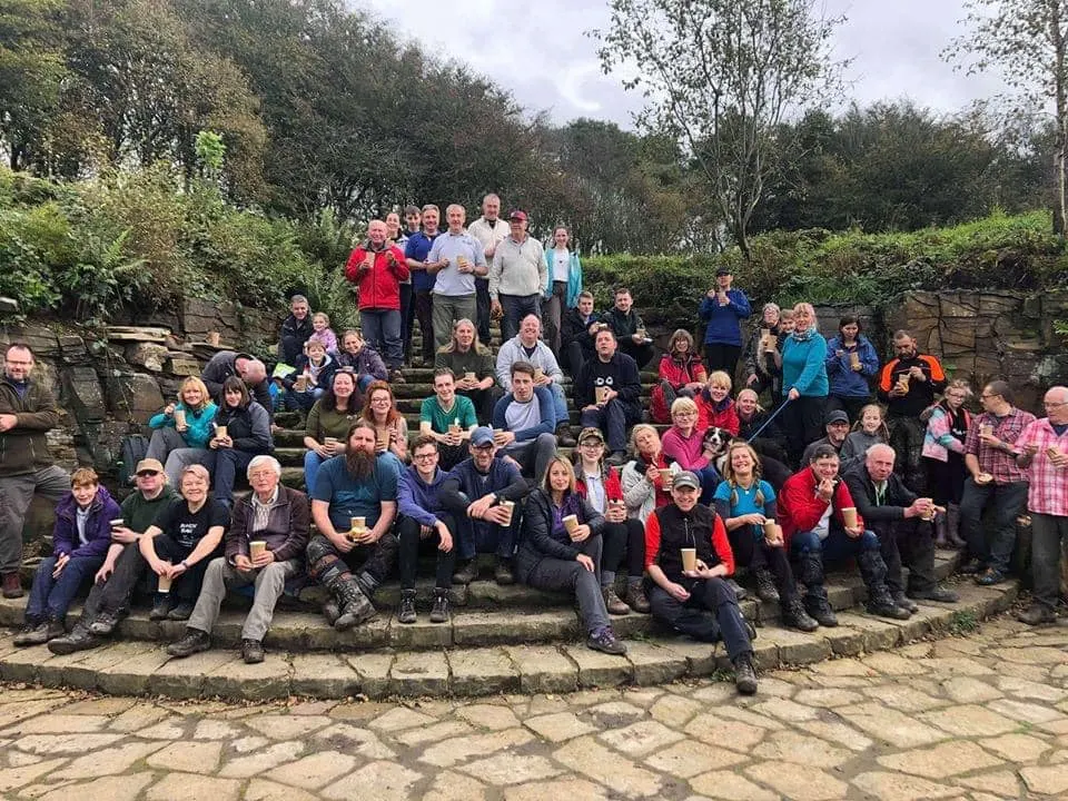 Large group of visitors gathered on stone steps in a wooded outdoor setting.