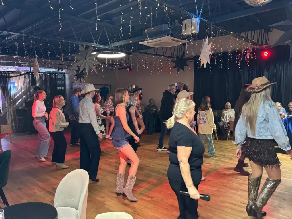 People dancing and socialising in an indoor venue with decorative hanging lights and western-themed décor.
