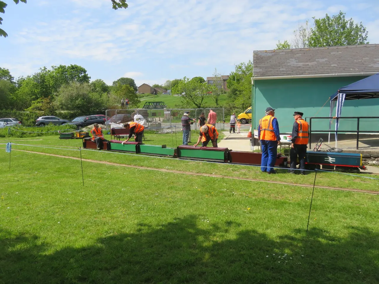 Staff and visitors operating miniature steam trains on a narrow-gauge track at an outdoor railway site.
