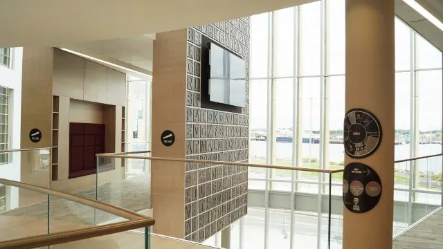 Modern interior space with tan columns, glass railing, decorative wall panels, and large windows overlooking countryside.