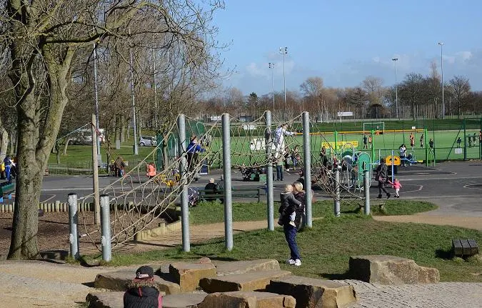 Children playing on climbing equipment and in outdoor play areas at a park on a sunny day.