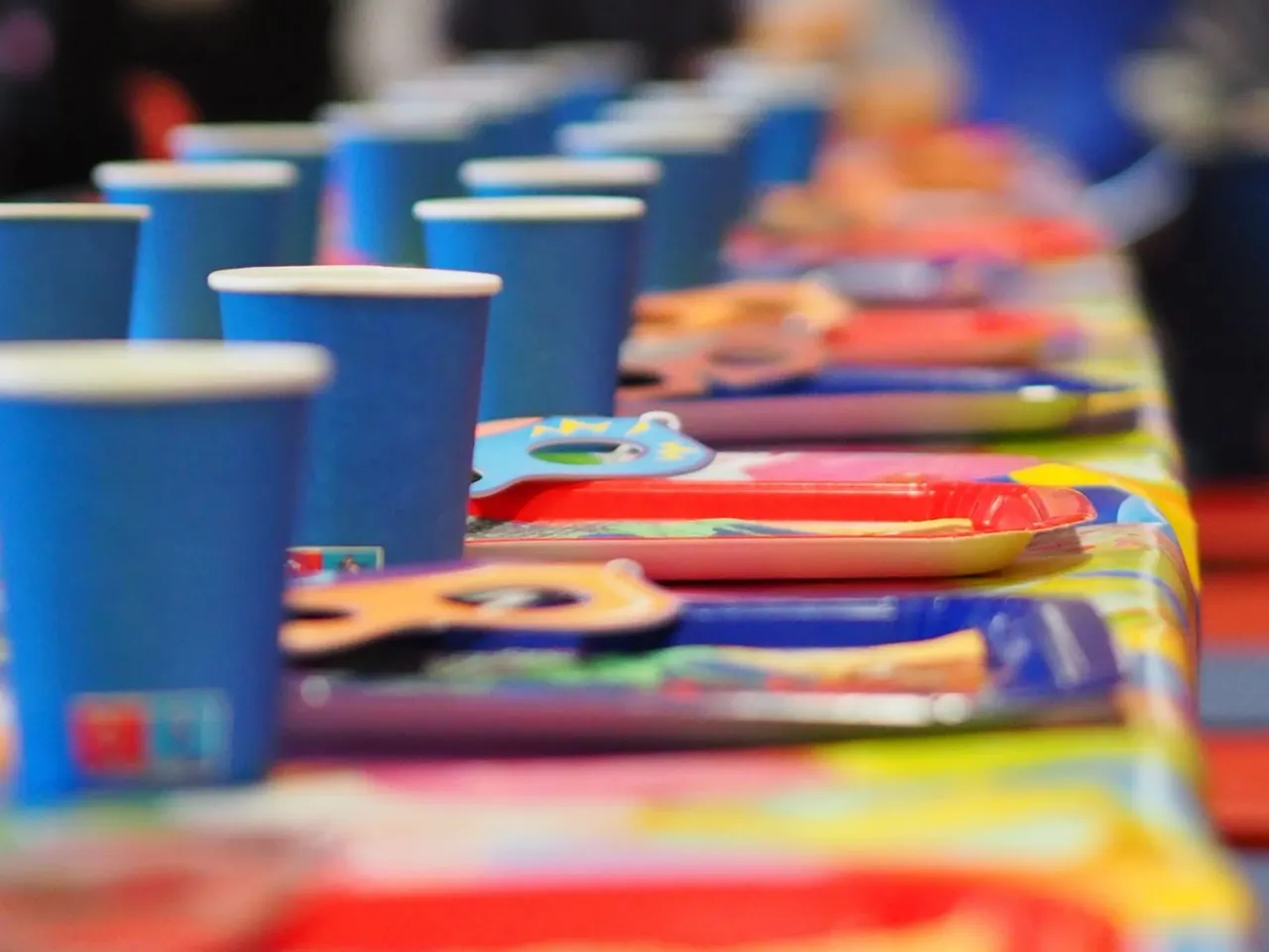 A row of blue cups and colourful children's place mats set out on tables for a party or group activity.