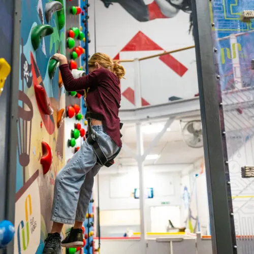 Child climbing an indoor climbing wall with colourful handholds in a leisure centre.