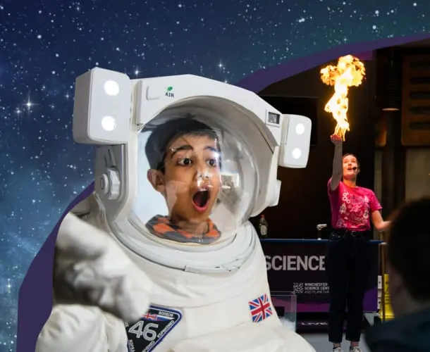 Child's face visible through astronaut helmet visor against starry backdrop, with fire breather performer in background.