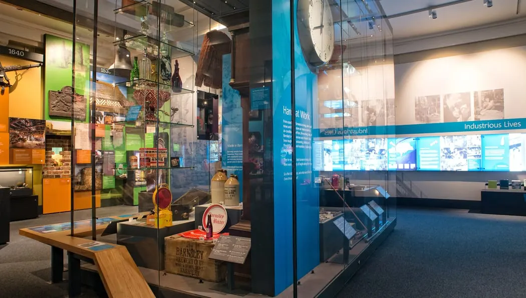 Museum interior with glass display cases containing historical artefacts, vintage bottles and industrial memorabilia, with interactive screens and wooden seating.