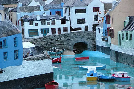 Colourful fishing boats moored in turquoise water surrounded by miniature whitewashed and blue buildings.