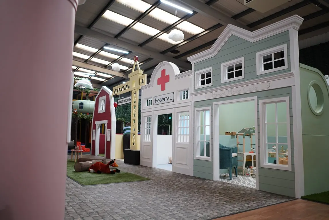 Indoor play area with colourful themed building structures including a hospital and construction site for children's play.