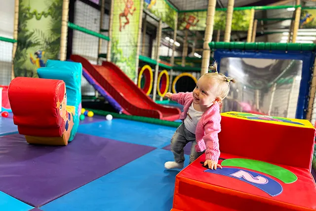 Toddler crawling through colourful soft play equipment in an indoor play centre.