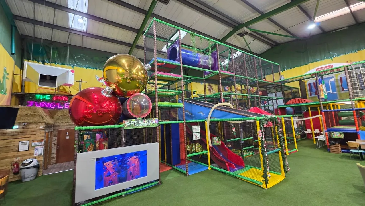 Colourful indoor play arena with multi-level soft play equipment, slides, climbing frames and giant decorative baubles.