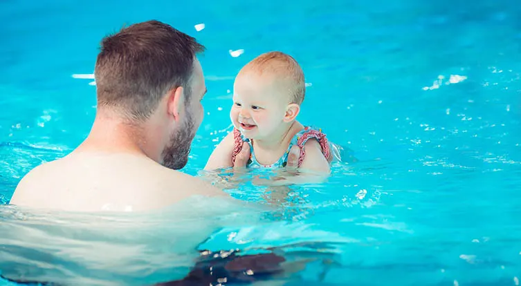 Adult and toddler playing together in a bright blue swimming pool.