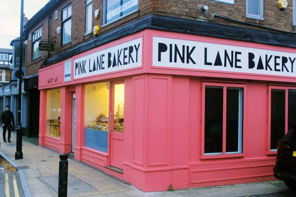 Bright pink bakery storefront on a street corner with display windows showing baked goods inside.