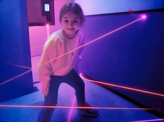 Child navigating through a laser maze game in a neon-lit indoor play area.