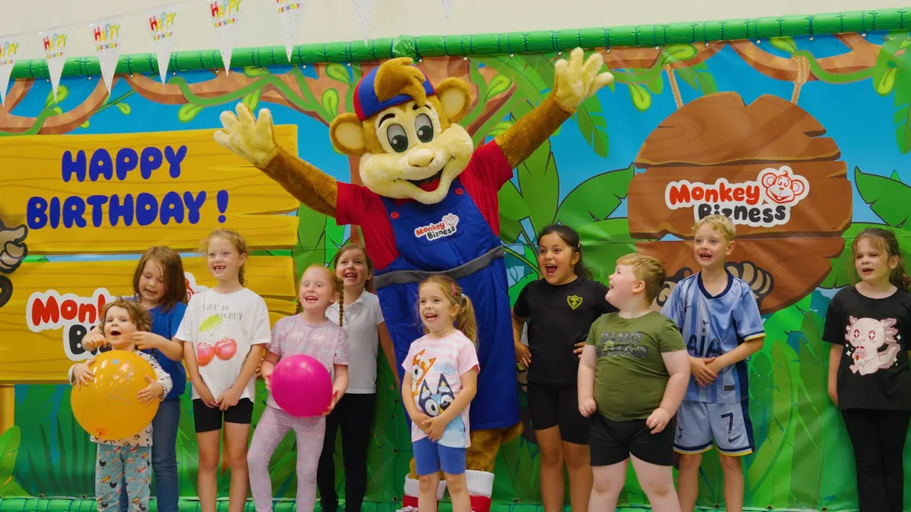 Group of children posing with a monkey mascot character at a birthday party celebration.