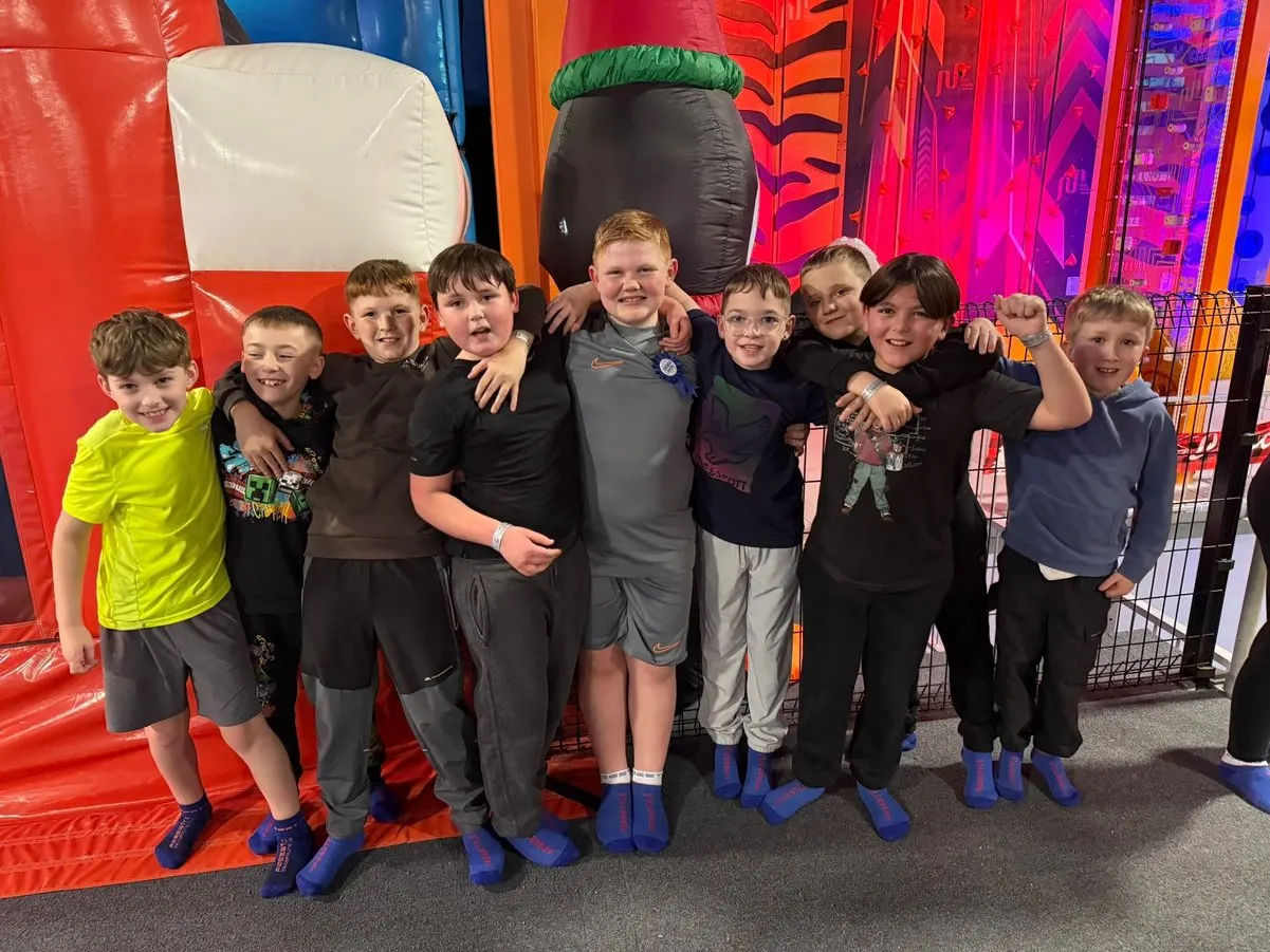 Group of children posing together in front of colourful inflatable bounce structures at an indoor trampoline park.