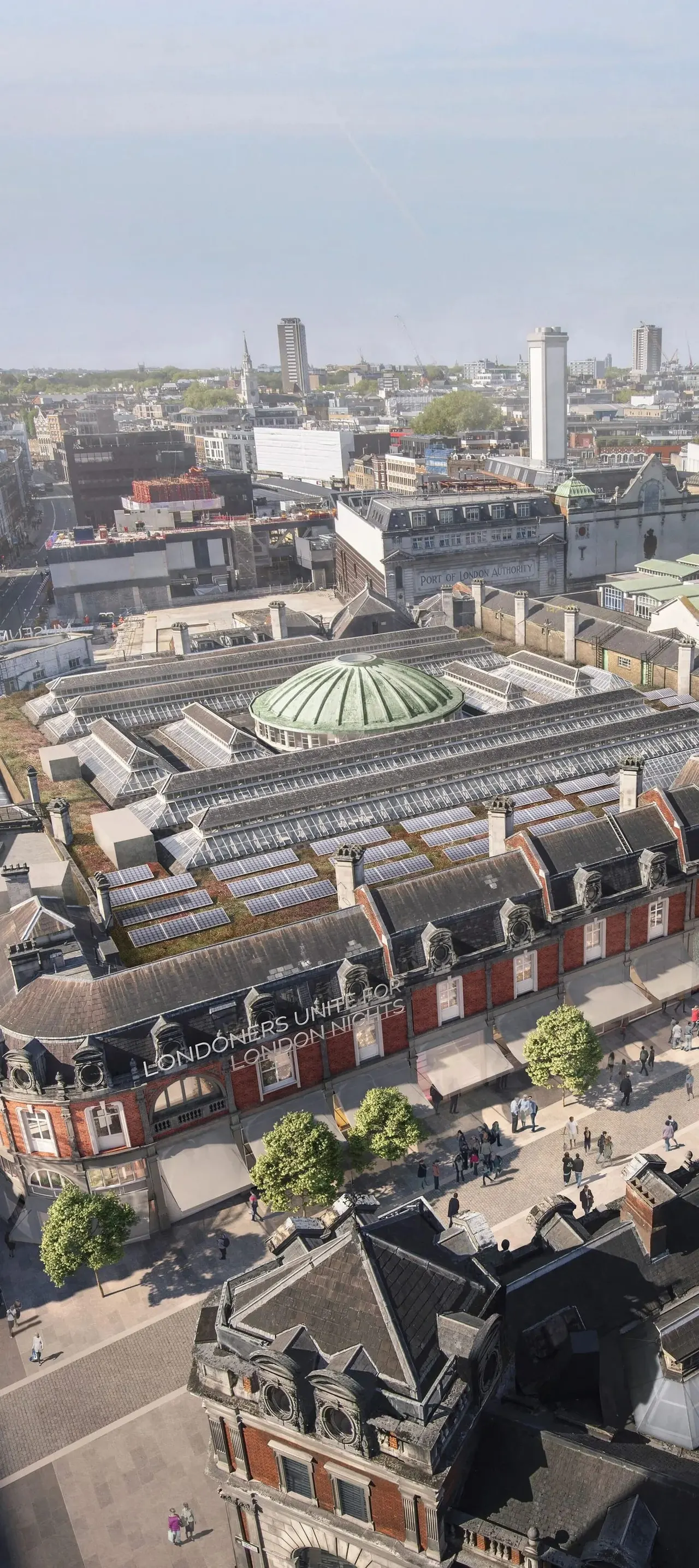 Aerial view of a historic brick building with solar panels on its roof, overlooking London's docklands and city skyline.