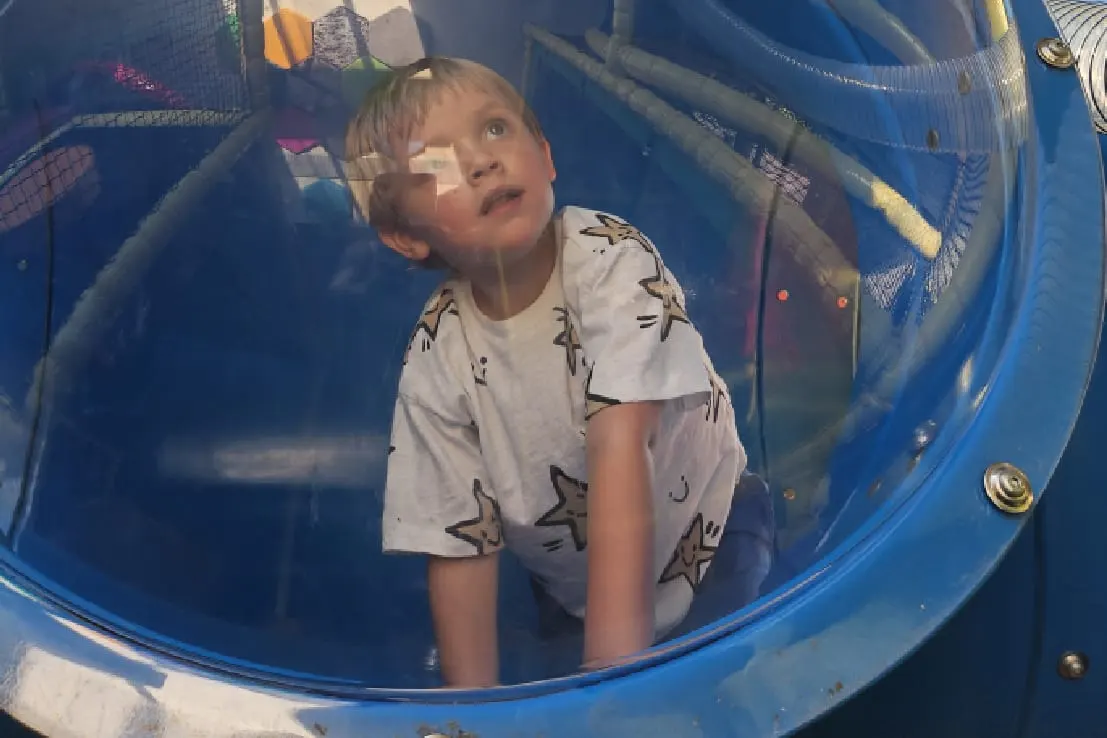 Young child inside a blue play tunnel or tube structure, looking upward.