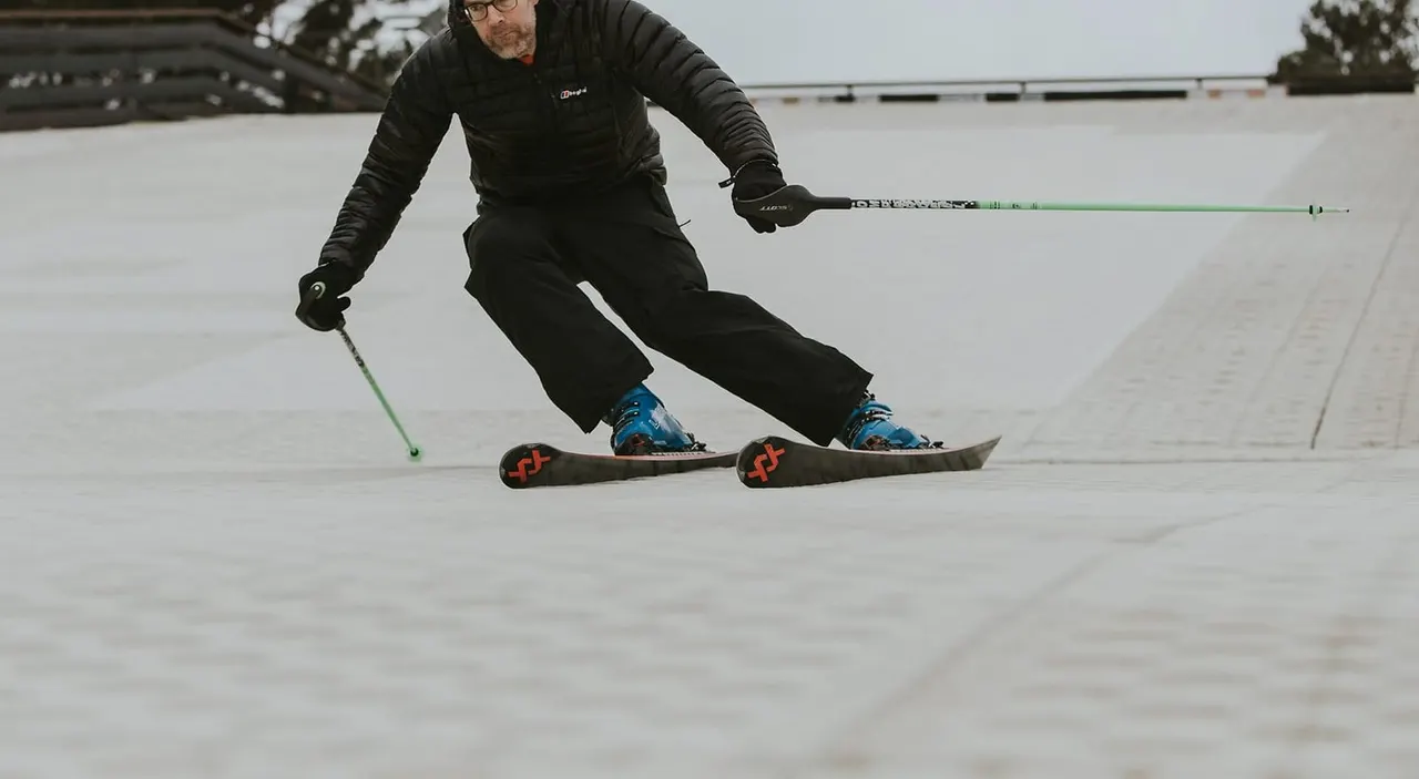 Man in black jacket and trousers skiing across frozen lake surface, holding green ski poles.