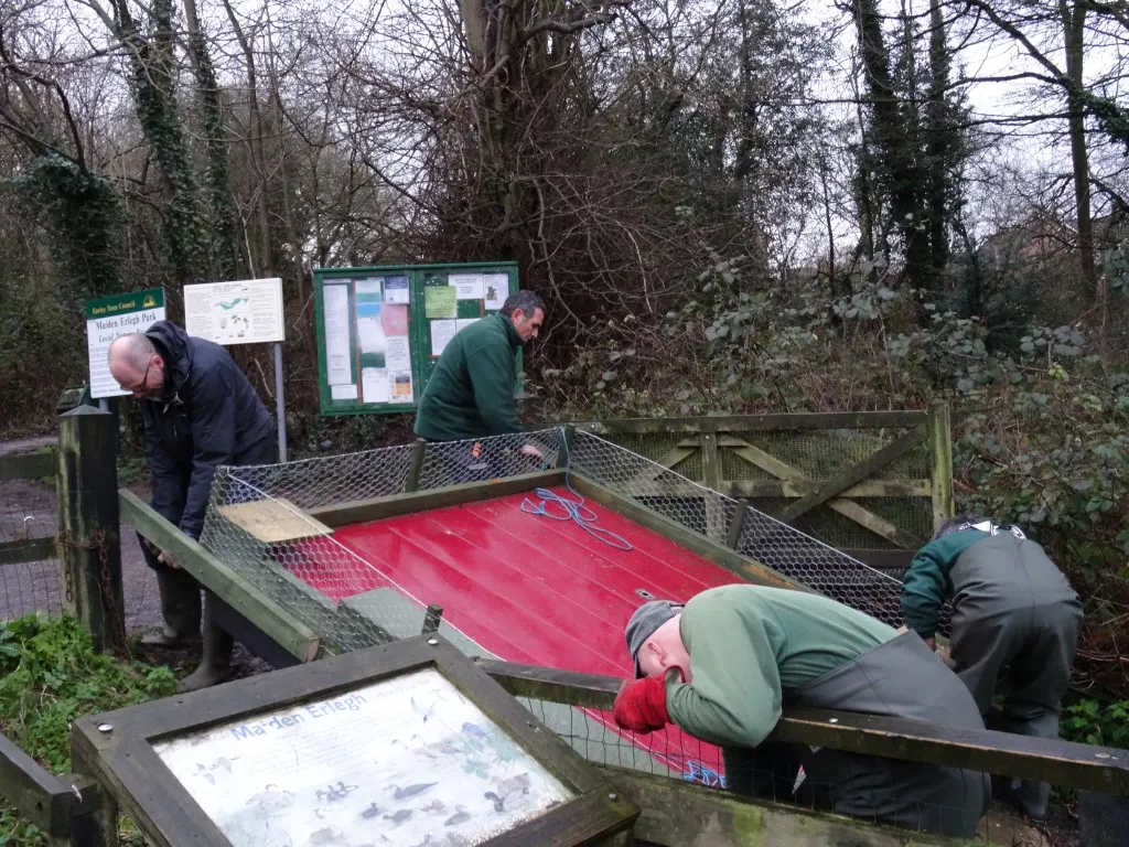 Visitors play miniature golf on a red course surrounded by bare winter trees and information boards at an outdoor leisure facility.