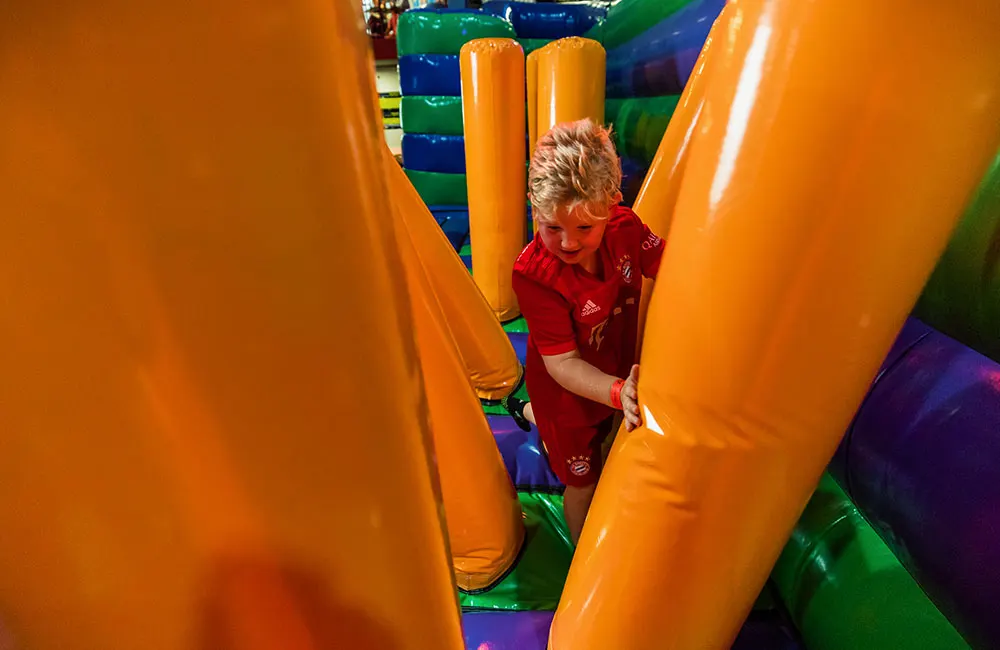 Young child navigating through inflatable obstacles inside a soft play structure.