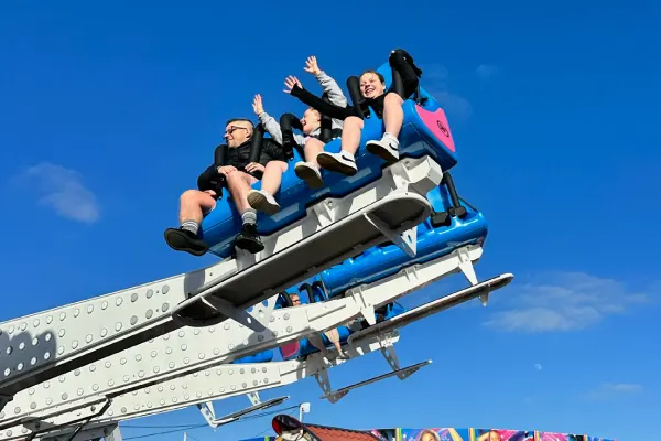 A group of people riding a blue roller coaster car against a clear blue sky.