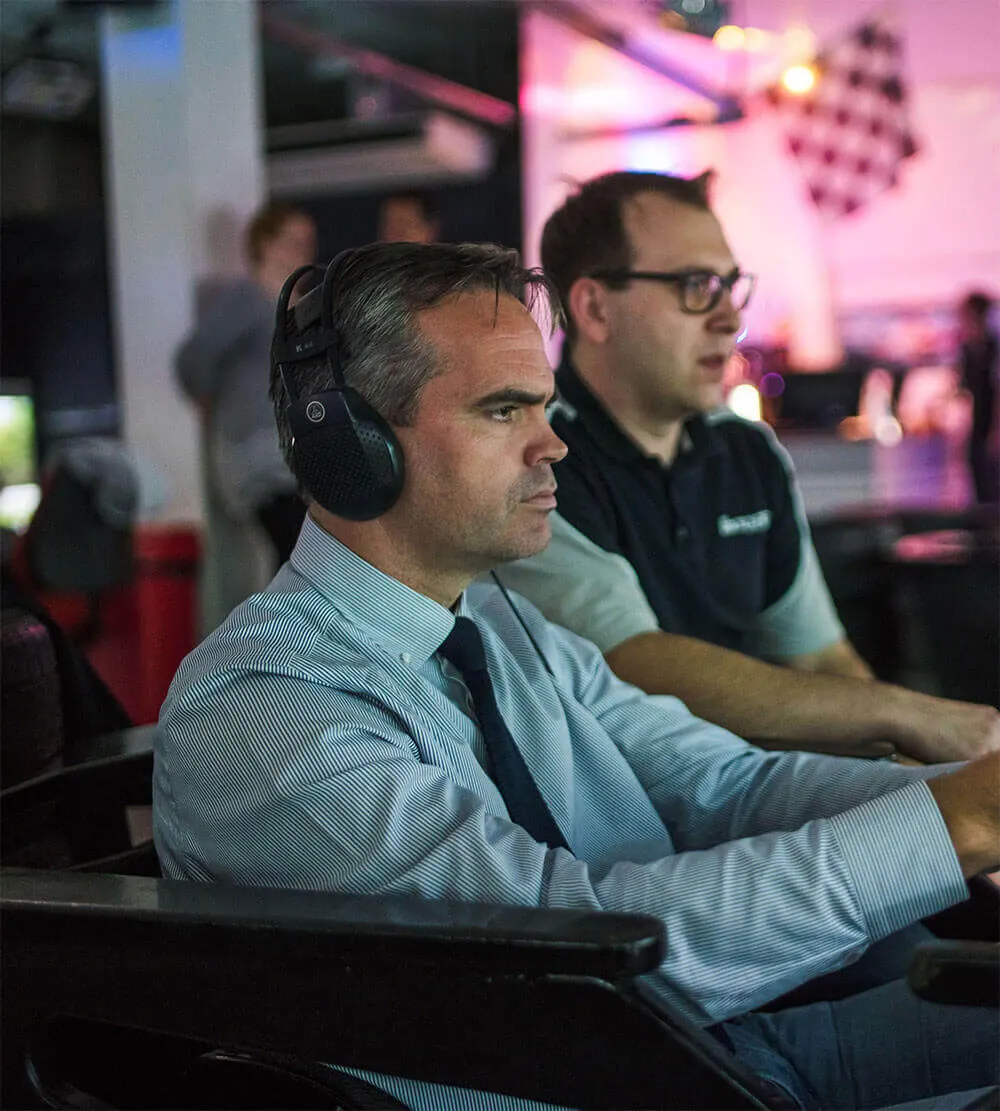 Two men gaming at racing simulators with headsets in a neon-lit arcade environment.