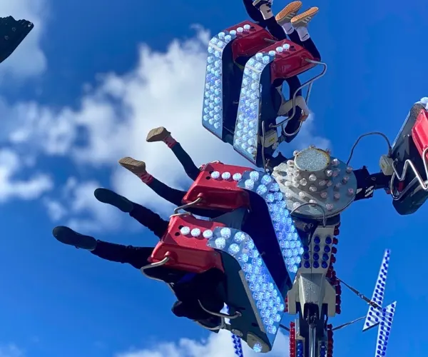 Fairground ride with red and blue mechanical arms carrying passengers against a bright blue sky.