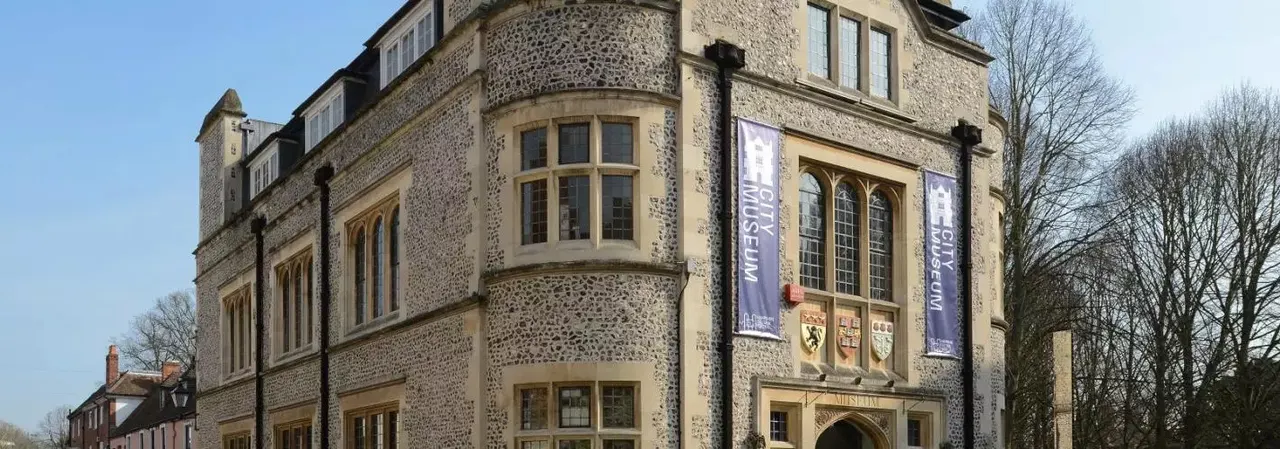 Historic stone building with turrets and large arched windows, displaying purple banners advertising the museum.