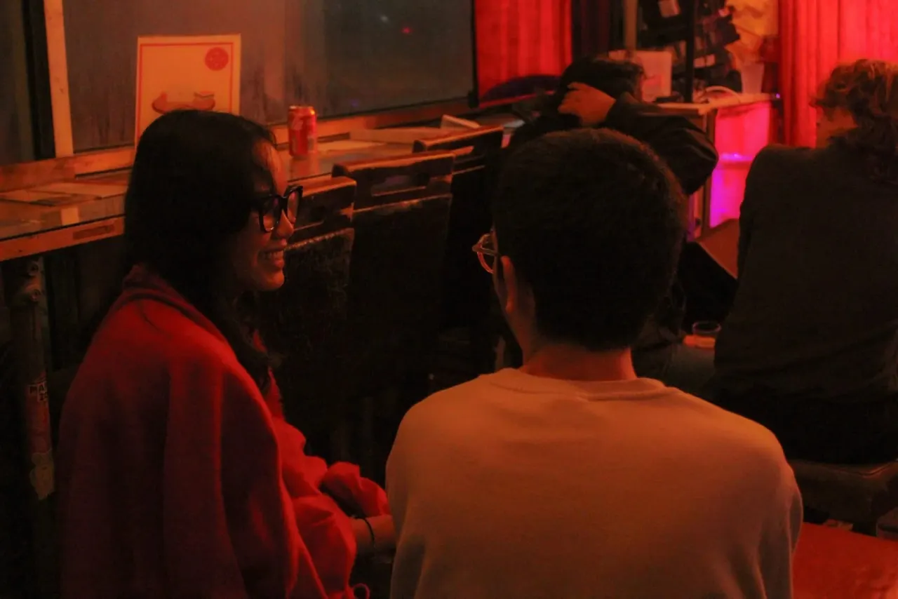 People playing pool in a dimly lit room with warm orange and red atmospheric lighting.