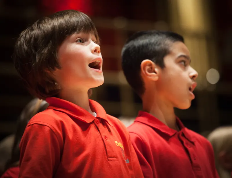 Two young children in red shirts singing with their mouths open, looking upwards.