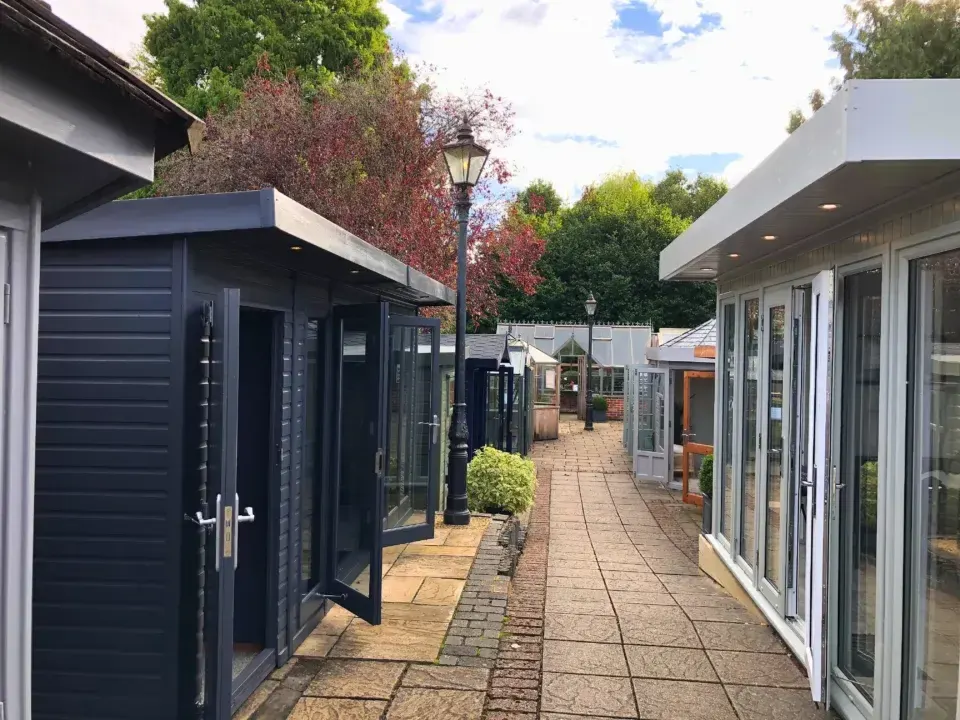 Modern garden rooms and studios line a brick-paved courtyard path lined with plants and autumn foliage.