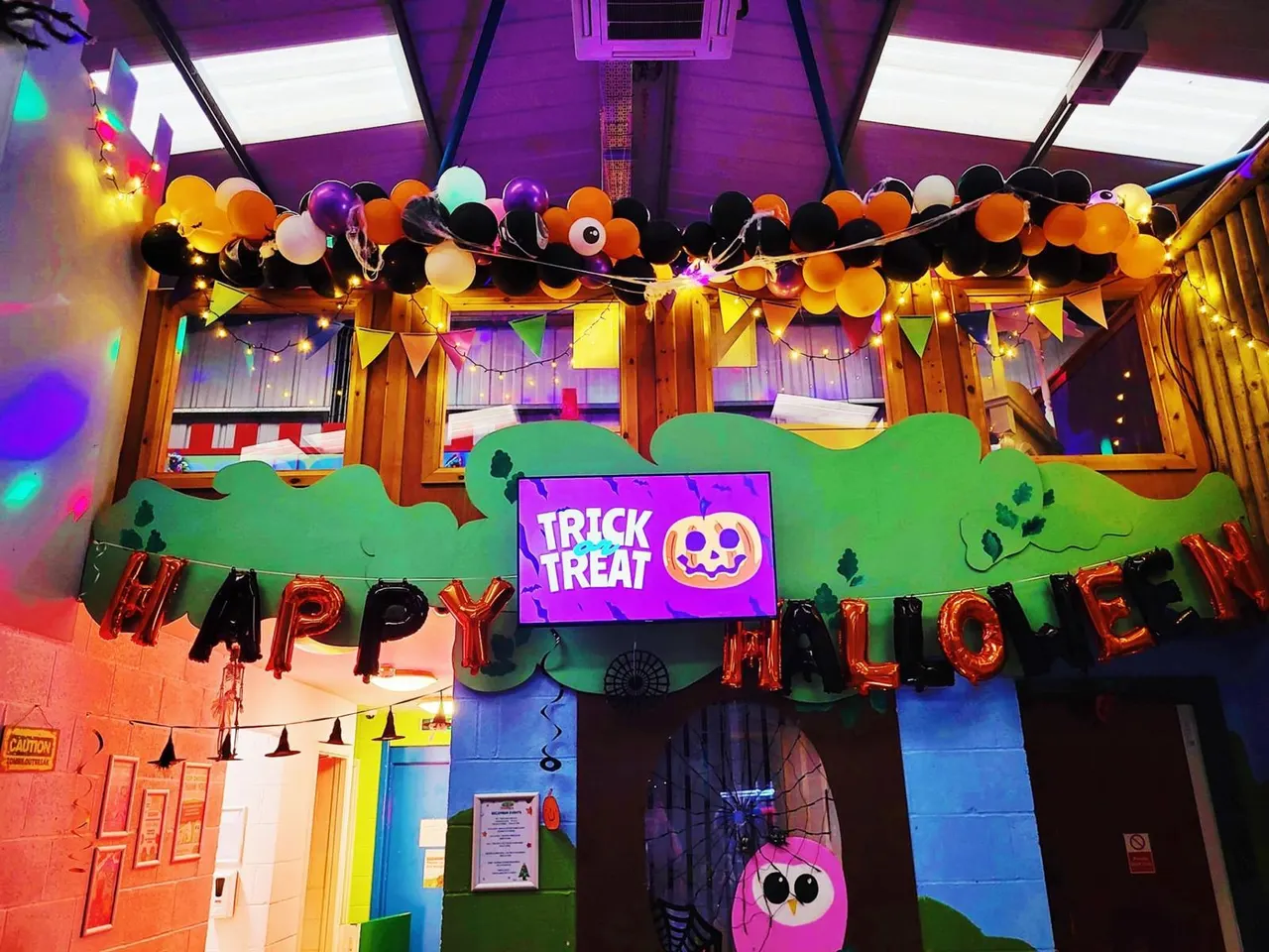 Halloween-themed indoor play area decorated with purple lighting, colourful balloons, bunting, and "Trick or Treat" signage.