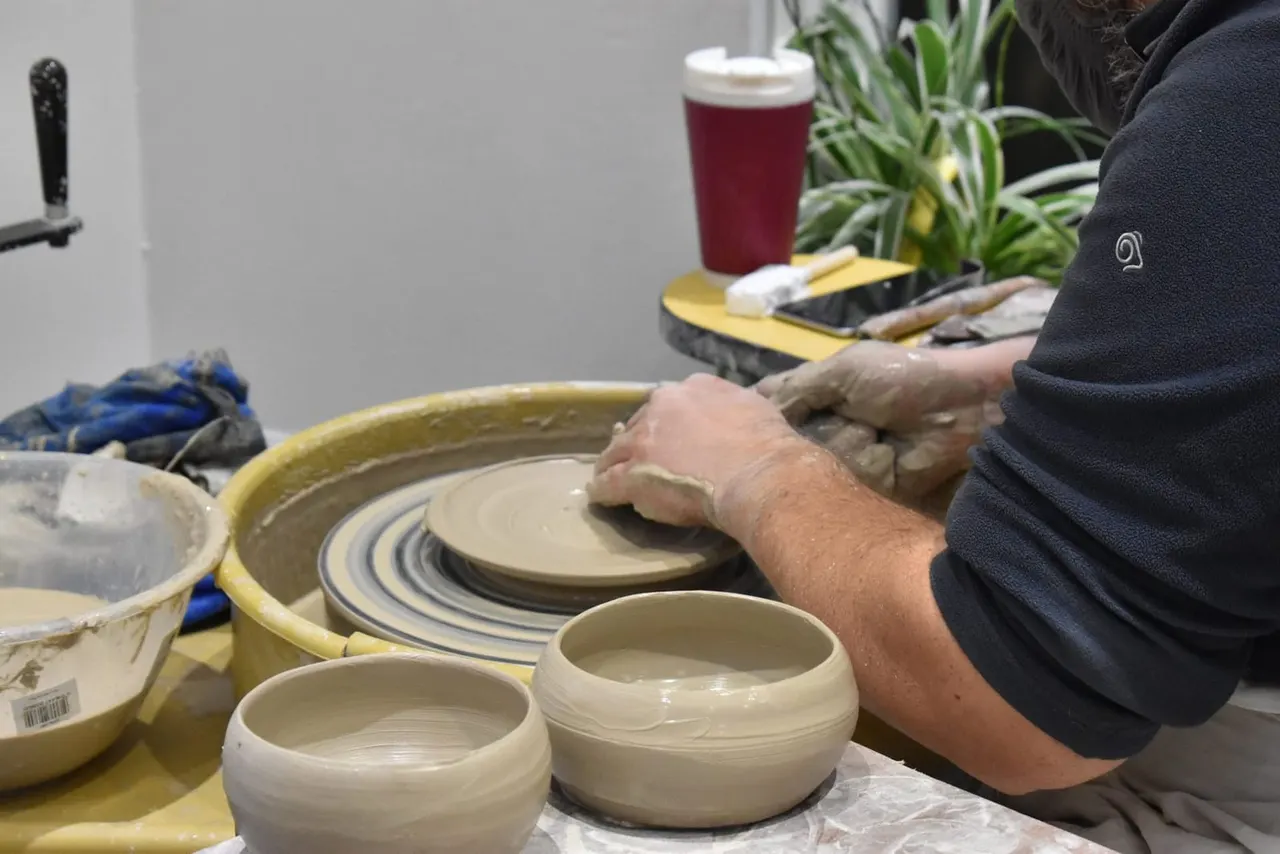 Person shaping clay on a pottery wheel during a ceramic workshop session.
