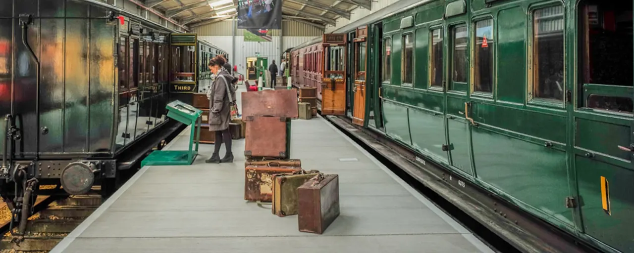 Vintage steam railway carriages and vintage suitcases displayed on a platform inside a heritage railway museum or station.