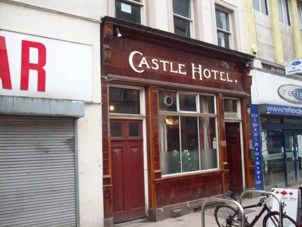 Victorian-era pub frontage with dark red wooden exterior, white signage, and street-level entrance between neighbouring shops.