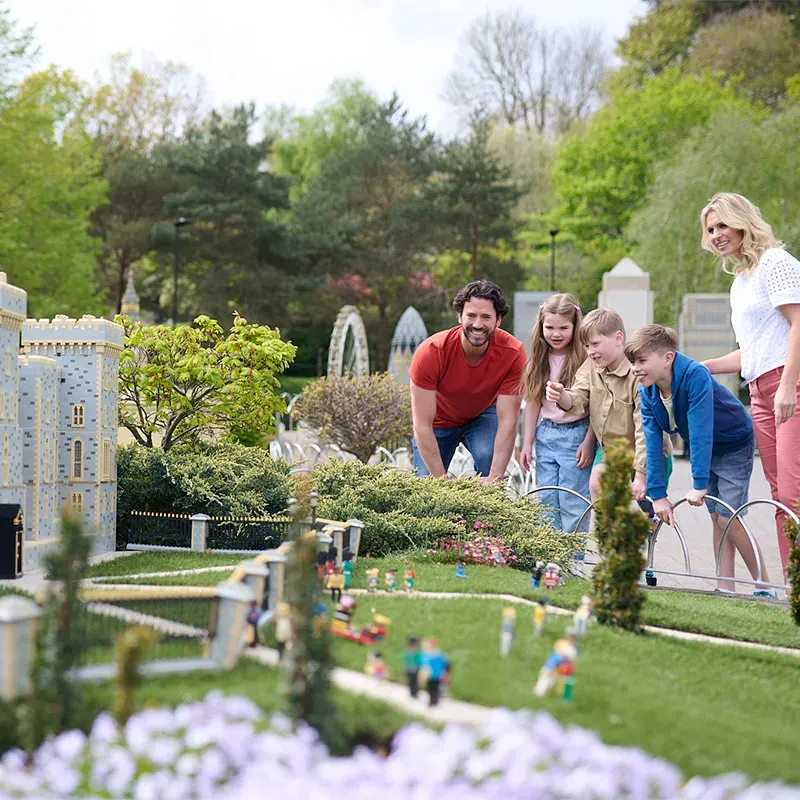 Family viewing a detailed miniature landscape model with buildings, gardens and figurines.