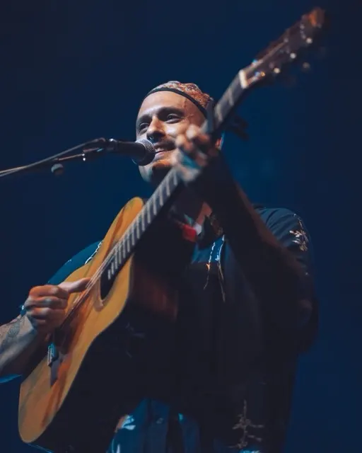 Male musician performing with acoustic guitar at microphone on stage.